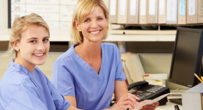 Zwei junge Krankenschwestern besprechen sich bei der Schichtübergabe