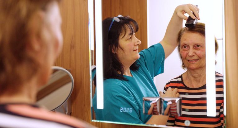 Eine Pflegekraft kämmt die Haare einer älteren Dame