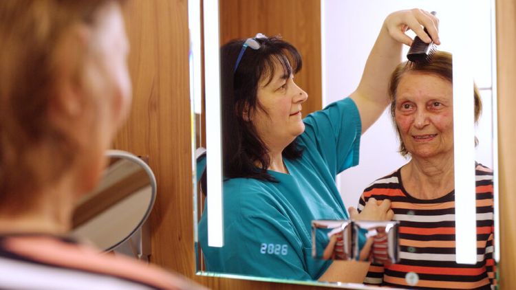 Eine Pflegekraft kämmt die Haare einer älteren Dame