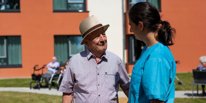 Senior und Pflegekraft unterhalten sich im Vorgarten der Seniorenresidenz