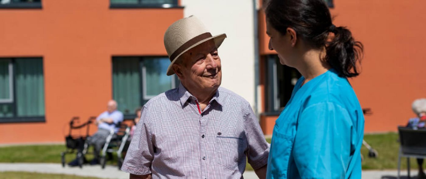 Senior und Pflegekraft unterhalten sich im Vorgarten der Seniorenresidenz