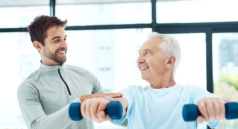 Therapeut unterstützt älteren männlichen Patienten beim Hanteltraining