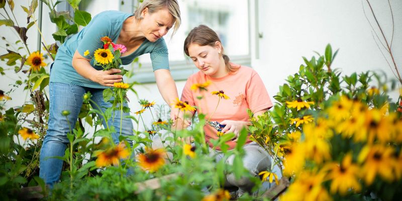Ein Mädchen und eine Erwachsene kümmern sich um die Pflege der Blumen im Garten