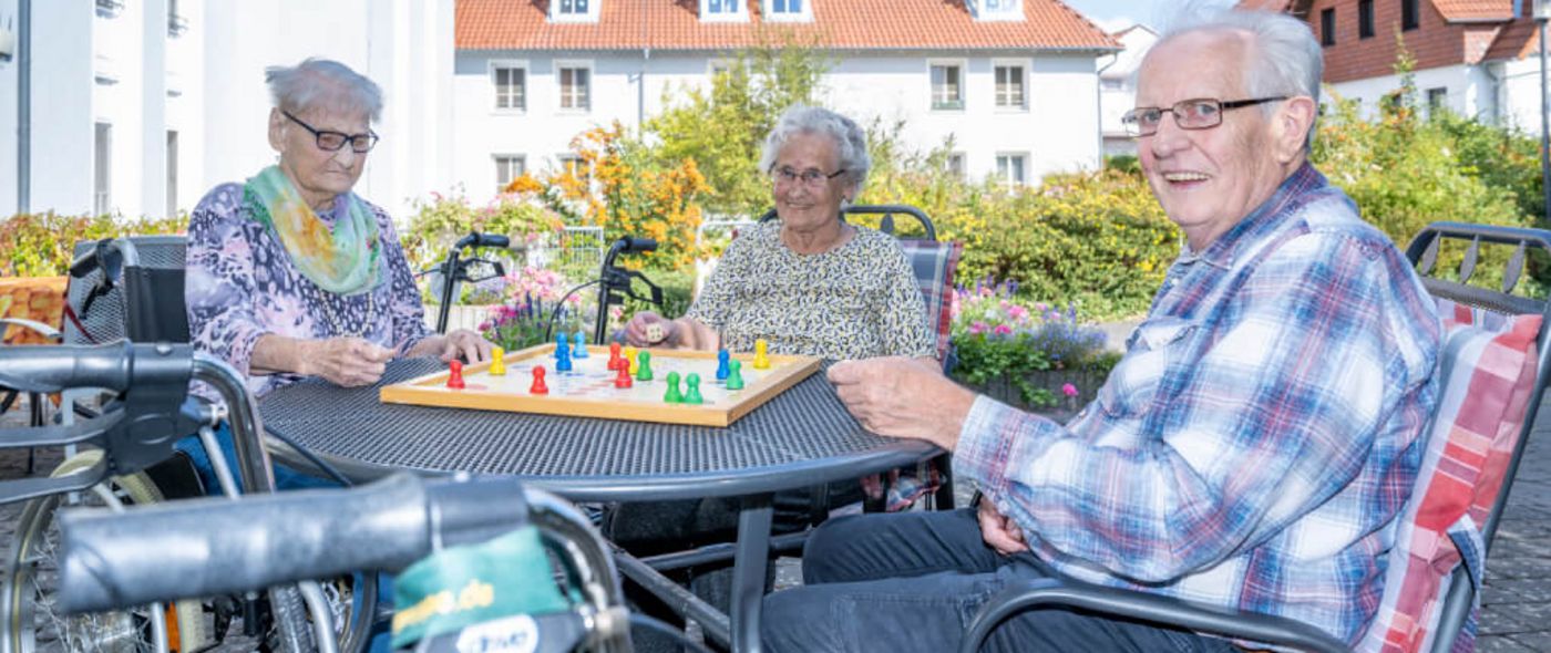 Senioren sitzen an einem Tisch draußen auf der Terrasse und spielen Mensch ärgere dich nicht