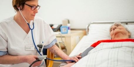 Pflegekraft misst den Blutdruck einer bettlägigen Patientin