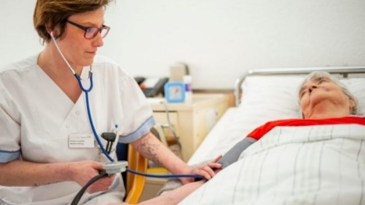 Pflegekraft misst den Blutdruck einer bettlägigen Patientin