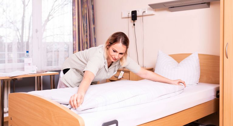 Eine Reinigungskraft von MEDICLIN richtet ein Patientenbett her.