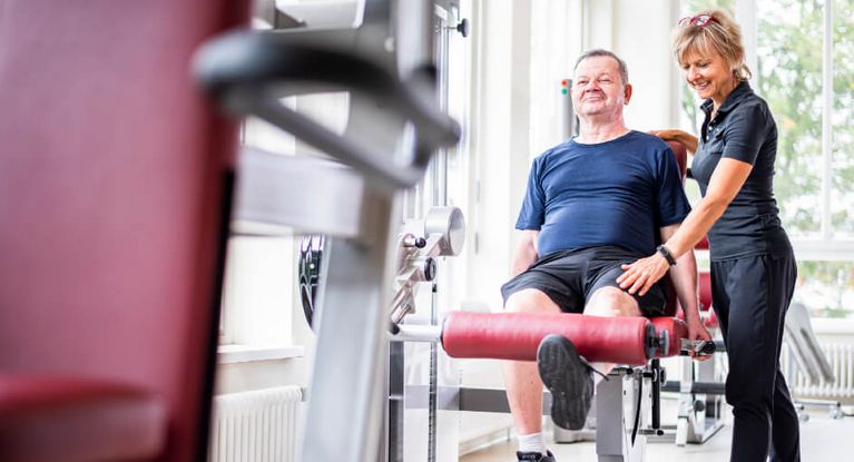 Therapeutin unterstützt Patienten bei der Beinpresse im MTT-Raum