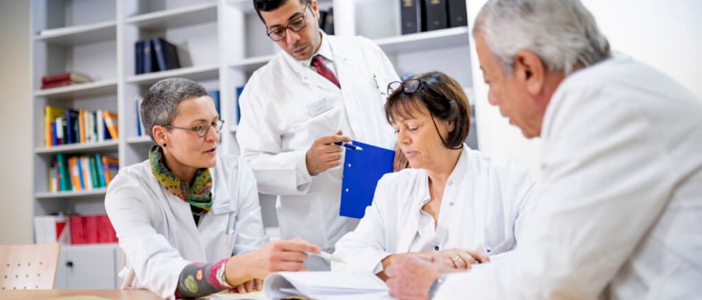 Ärztinnen und Ärzte sitzen gemeinsam an einem Tisch und besprechen eine Patientenakte